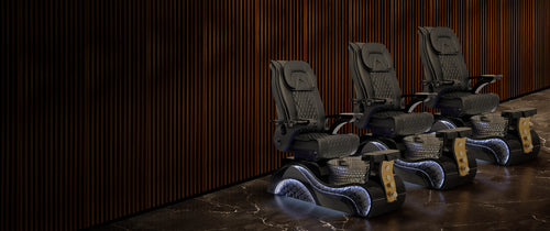 Three Lucent II Gold Edition pedicure chairs in black leather with gold accents and LED lit bases in a luxury nail salon